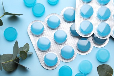 Photo of Many cough drops and eucalyptus on light blue background, flat lay