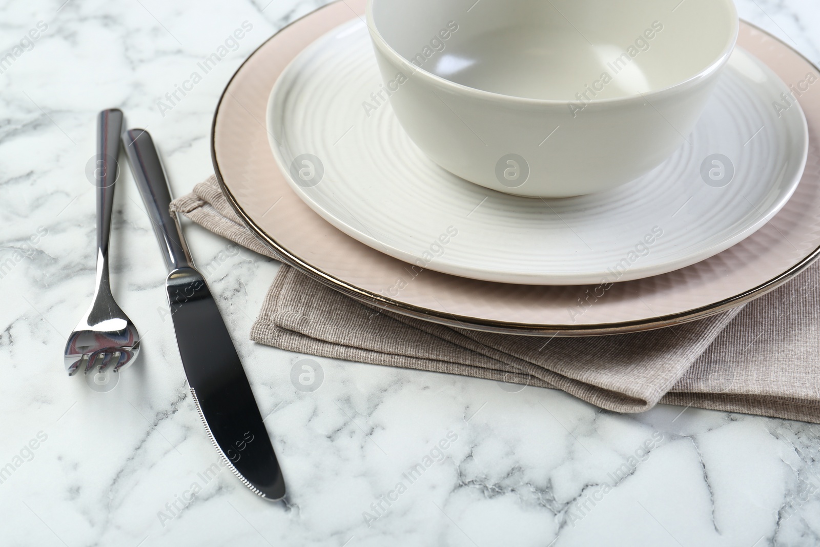 Photo of Clean plates, bowl, cutlery and napkin on white marble table, closeup