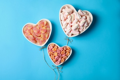 Photo of Twine near heart shaped bowls full of sweets imitating balloons on light blue background, top view