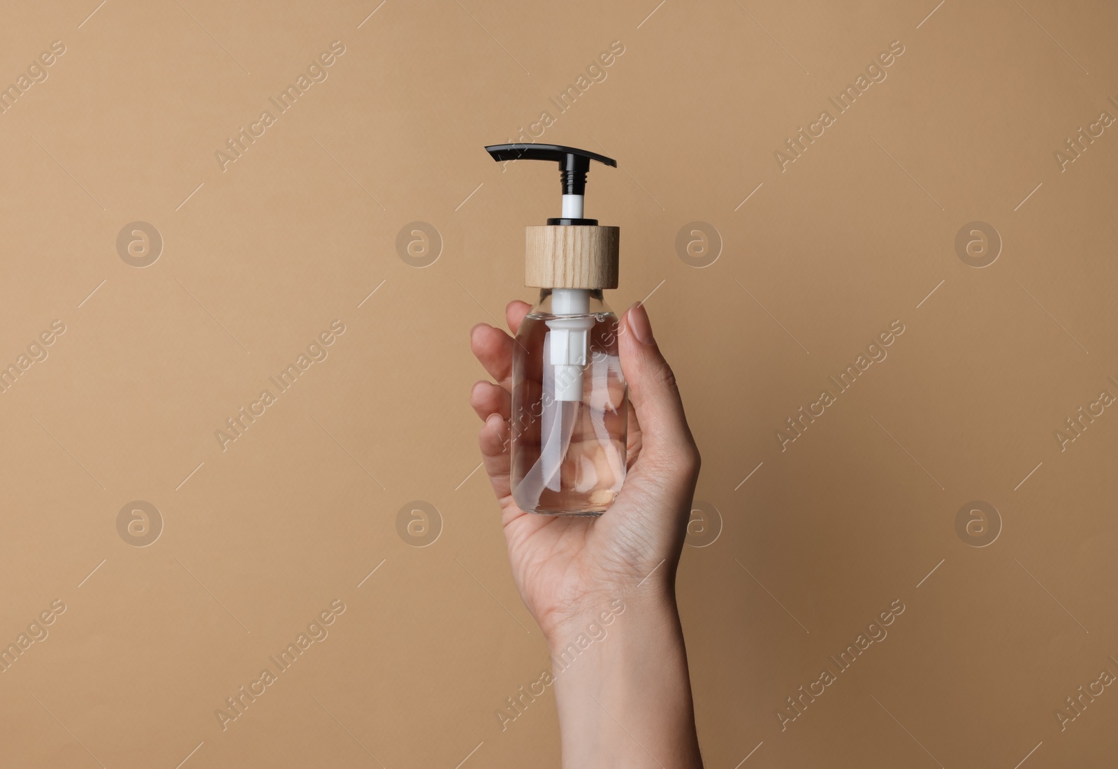 Photo of Woman holding bottle of cosmetic product on beige background, closeup