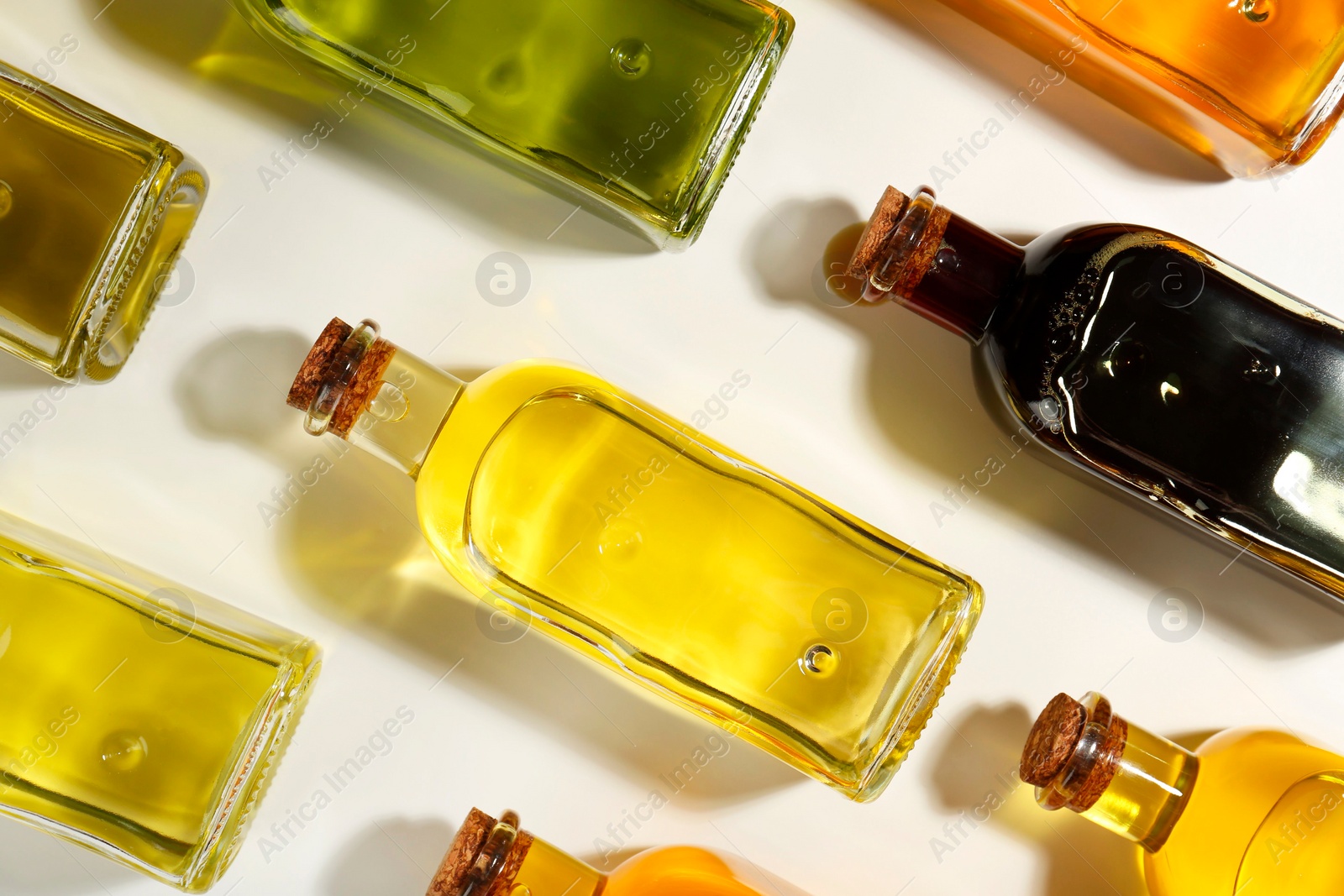 Photo of Vegetable fats. Different cooking oils in glass bottles on white background, flat lay