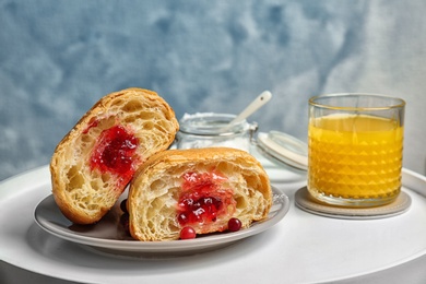 Tasty croissant with jam and glass of juice on table