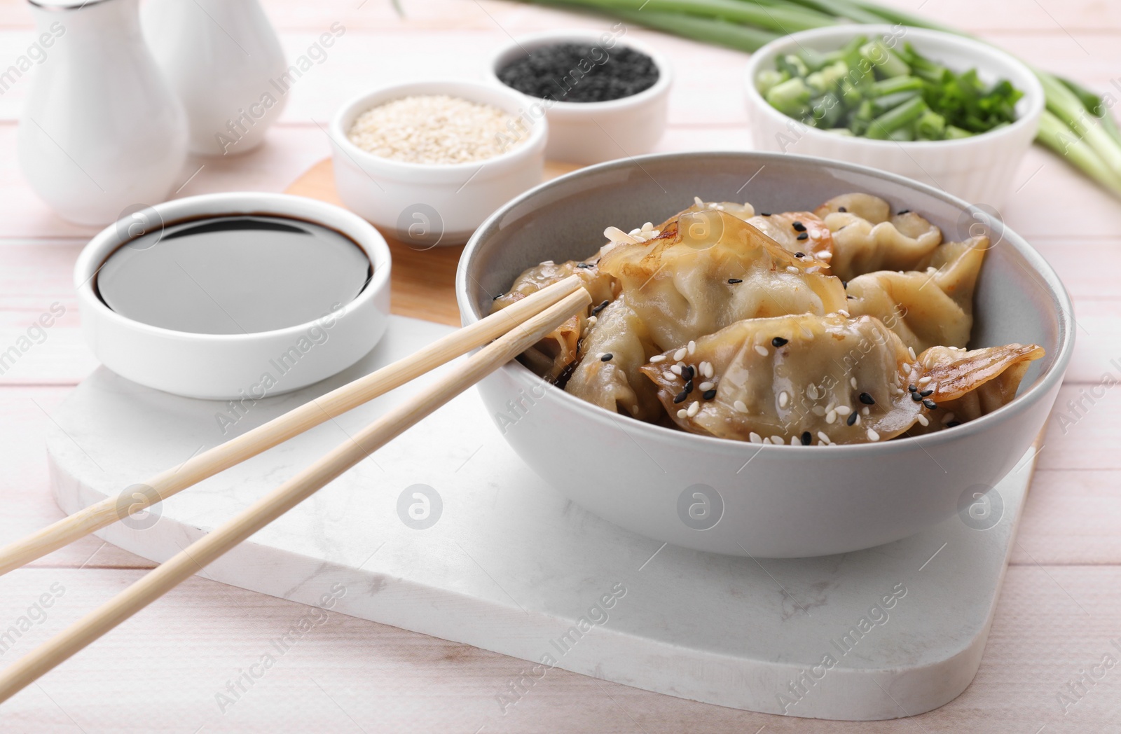 Photo of Delicious gyoza (asian dumplings) with sesame, soy sauce and chopsticks on white wooden table