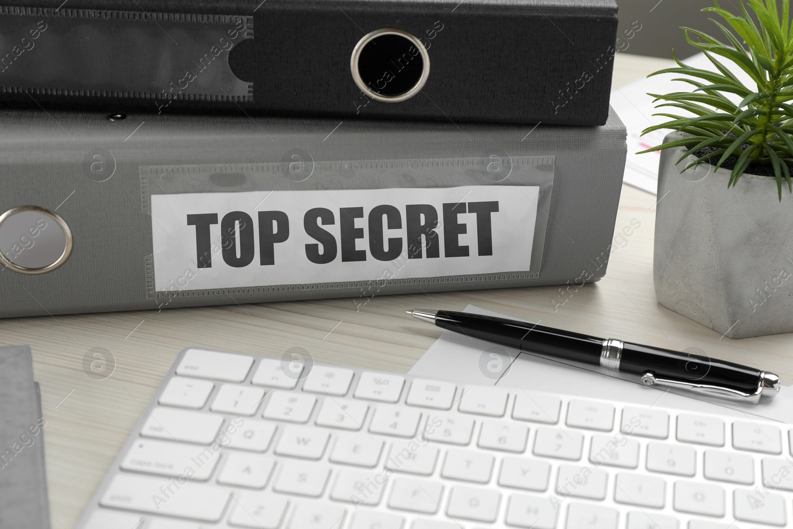 Image of Top Secret stamp. Folders, computer keyboard, pen and houseplant on white wooden table, closeup