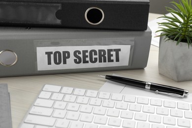 Image of Top Secret stamp. Folders, computer keyboard, pen and houseplant on white wooden table, closeup