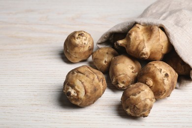 Photo of Sack with fresh Jerusalem artichokes on white wooden table, closeup. Space for text