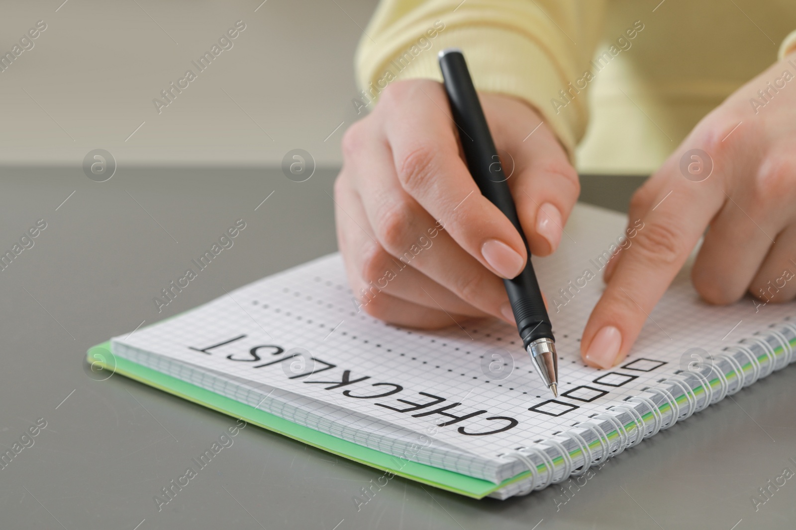 Photo of Woman filling Checklist with pen at grey table, closeup