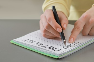 Woman filling Checklist with pen at grey table, closeup