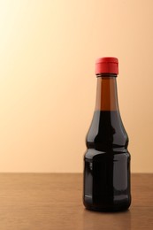 Photo of Bottle of soy sauce on wooden table against beige background