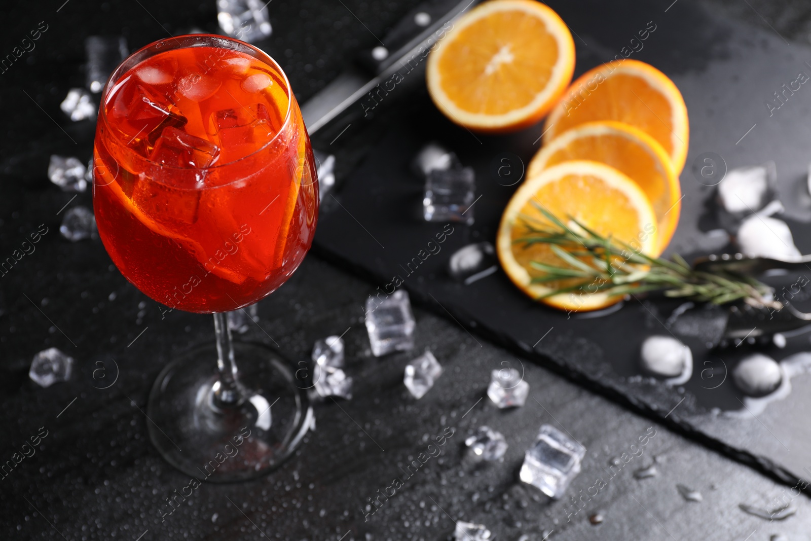 Photo of Glass of tasty Aperol spritz cocktail with orange slices and ice cubes on dark gray table, closeup