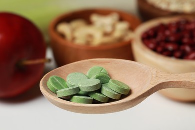 Photo of Wooden spoon of pills over foodstuff, closeup. Prebiotic supplements