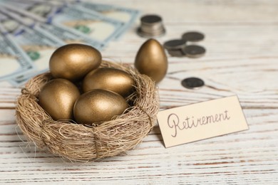 Photo of Golden eggs, money and card with word Retirement on white wooden table. Pension concept