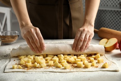 Photo of Woman making delicious apple strudel at table, closeup