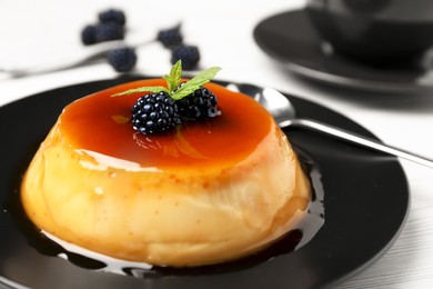 Plate of delicious caramel pudding with blackberries and mint served on white table, closeup