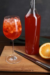 Photo of Aperol spritz cocktail and ice cubes in glass and bottle on wooden table