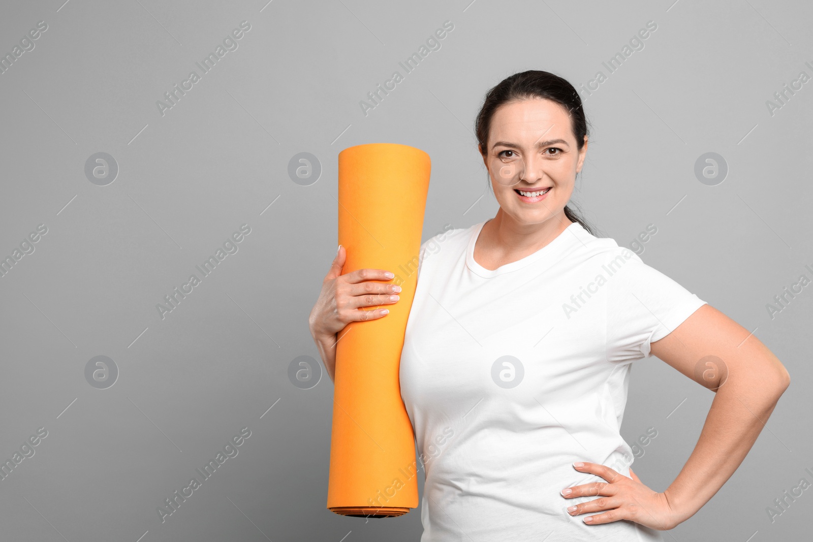 Photo of Happy overweight woman with yoga mat on grey background, space for text