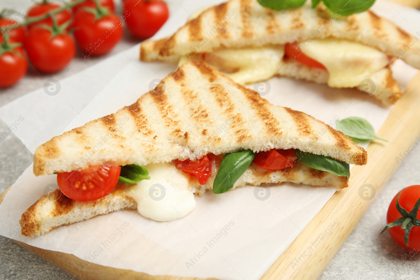Photo of Delicious grilled sandwiches with mozzarella, tomatoes and basil on wooden board, closeup