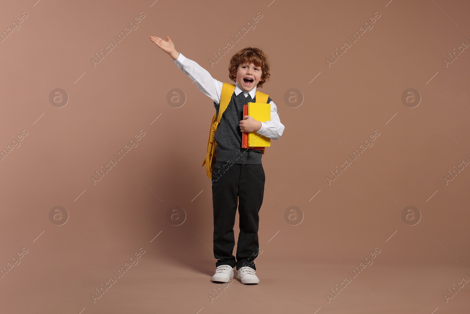 Photo of Emotional schoolboy with backpack and books on brown background