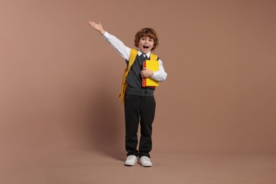 Emotional schoolboy with backpack and books on brown background