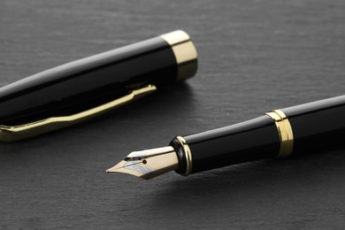 Photo of Stylish fountain pen and cap on dark textured table, closeup
