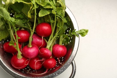 Photo of Wet radish in colander on white table, top view. Space for text