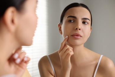 Photo of Woman with dry skin looking at mirror in bathroom