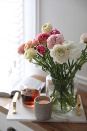 Photo of Bouquet of beautiful ranunculuses, candle and tea on cabinet in room