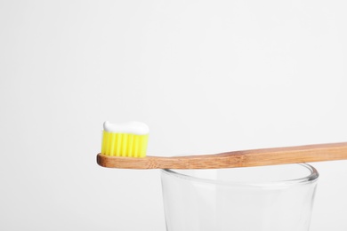 Bamboo toothbrush with paste on glass against white background