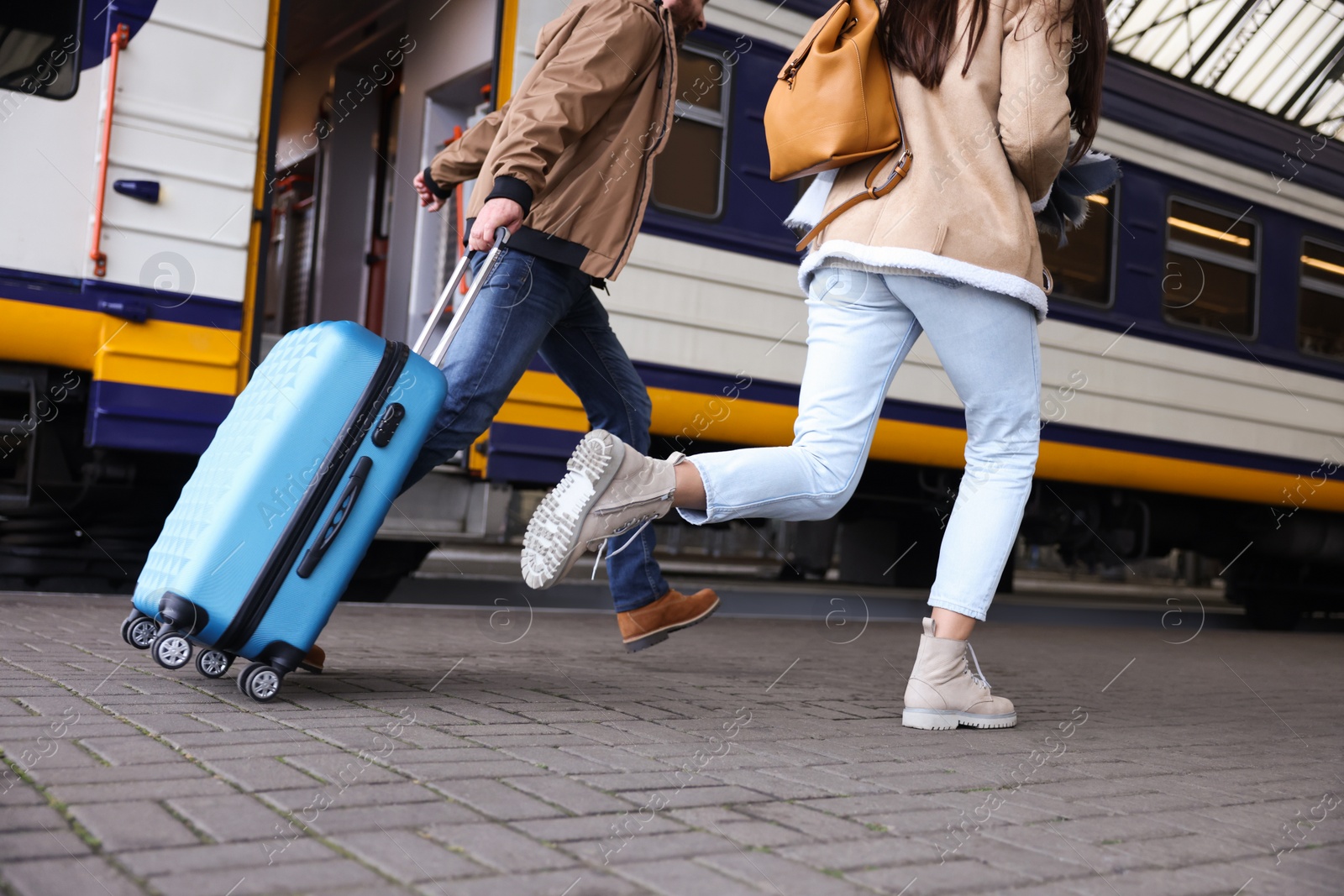 Photo of Being late. Couple with suitcase running towards train at station, closeup