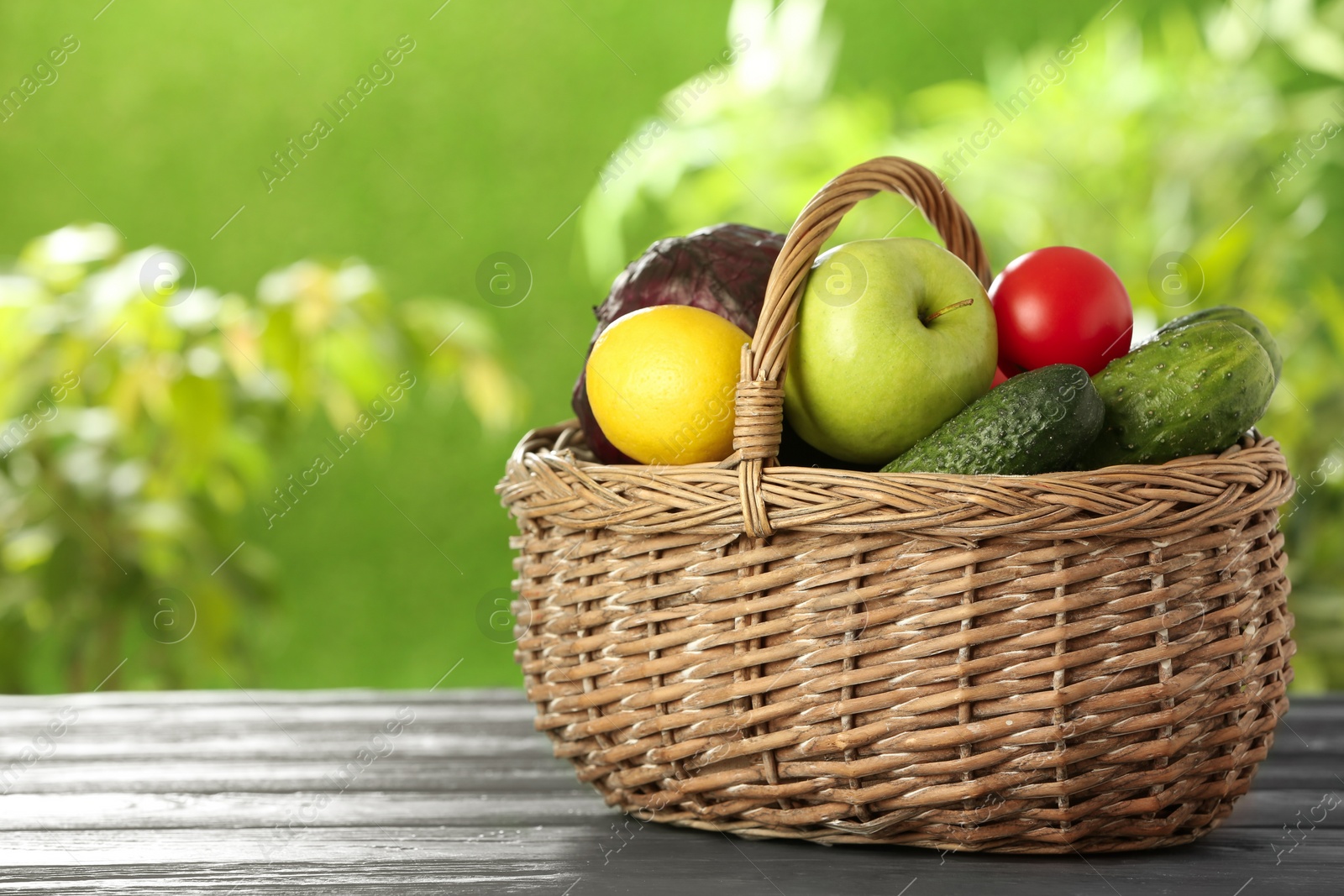Photo of Basket full of fresh vegetables and fruits on table outdoors, space for text