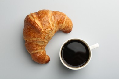 Photo of Delicious fresh croissant and cup of coffee on light background, flat lay