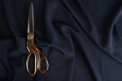 Photo of Scissors on dark blue fabric, top view. Space for text