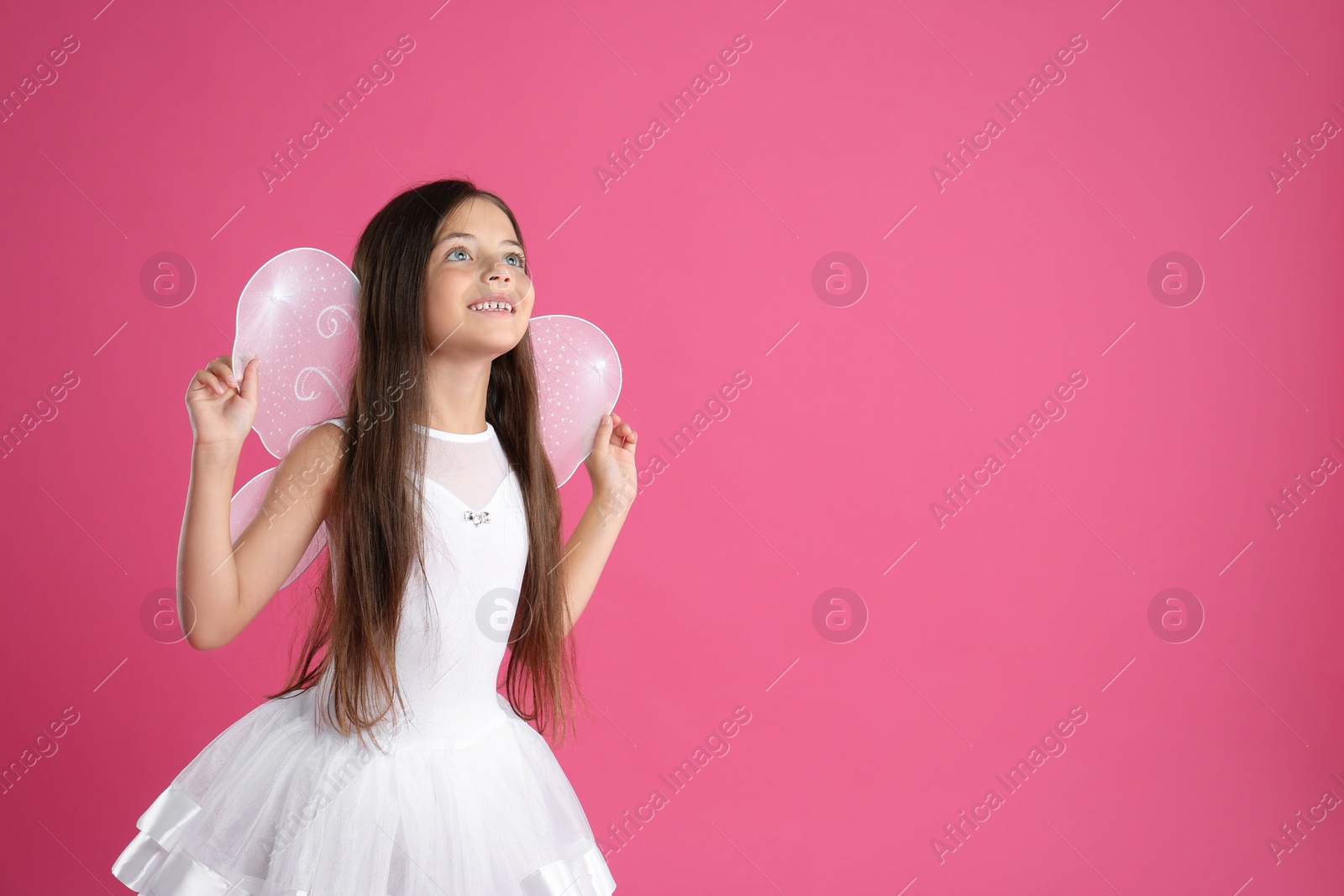 Photo of Cute little girl in fairy costume with wings on pink background. Space for text