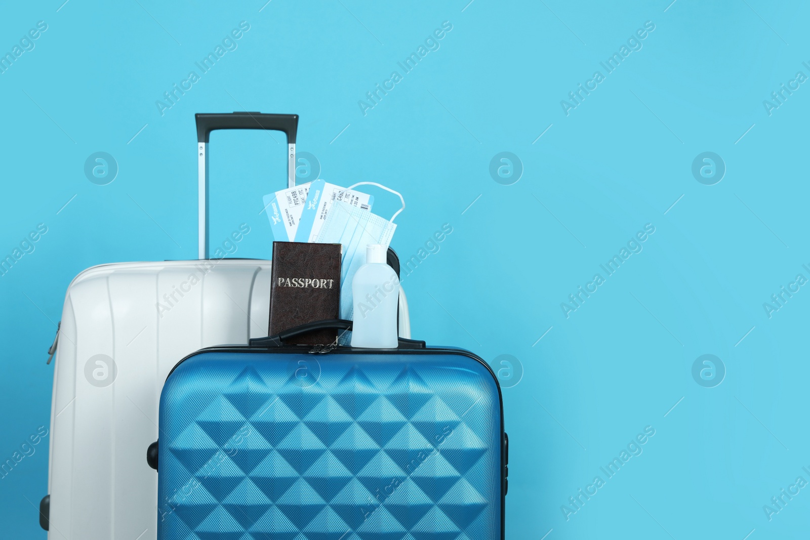 Photo of Passport with tickets, sanitizer and protective mask on suitcase against light blue background, space for text. Travel during quarantine