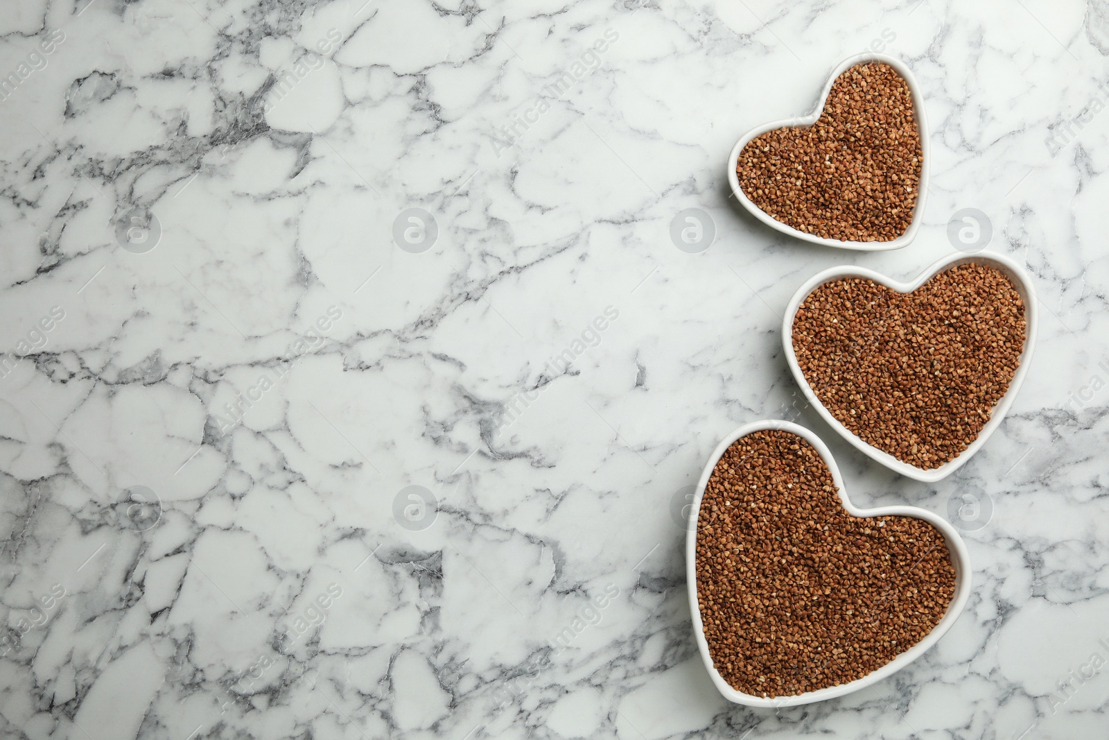 Photo of Buckwheat grains on white marble table, flat lay. Space for text