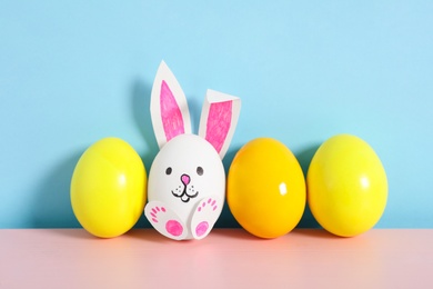 Photo of Bright eggs and white one as cute bunny on pink wooden table against light blue background. Easter celebration