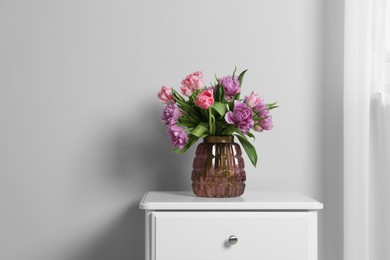 Photo of Beautiful bouquet of colorful tulip flowers on white bedside table near white wall