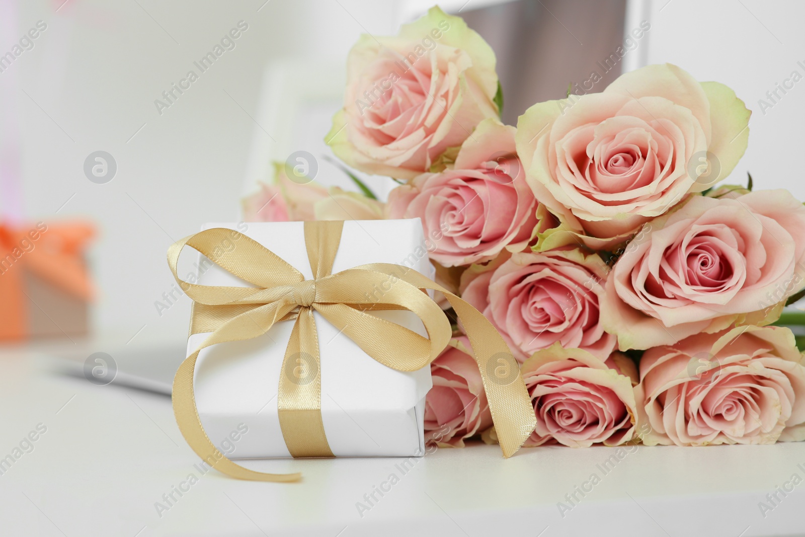 Photo of Beautiful bouquet of roses and gift on white table in room. Happy birthday greetings