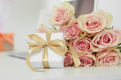 Photo of Beautiful bouquet of roses and gift on white table in room. Happy birthday greetings
