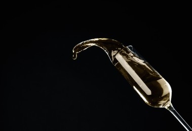 Sparkling wine splashing out of glass on black background