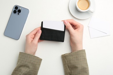 Woman holding leather business card holder with blank card at white table, top view