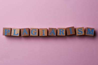 Photo of Wooden cubes with word Plagiarism on pink background, flat lay