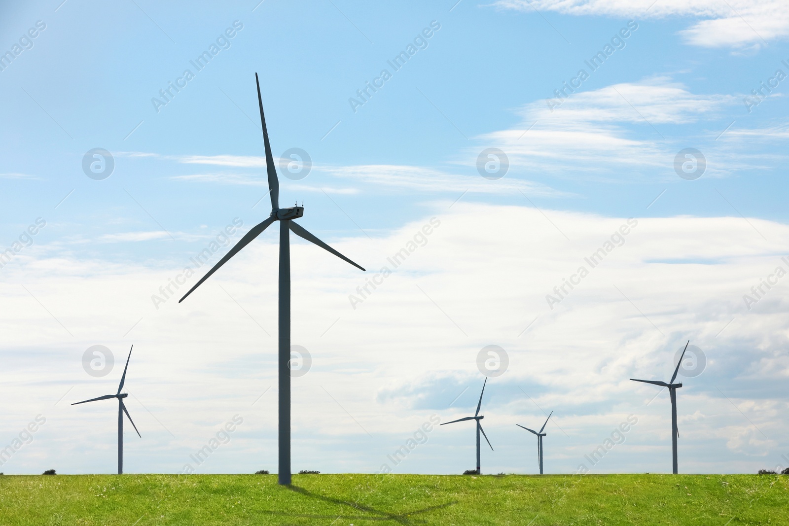 Image of Alternative energy source. Wind turbines in field under blue sky