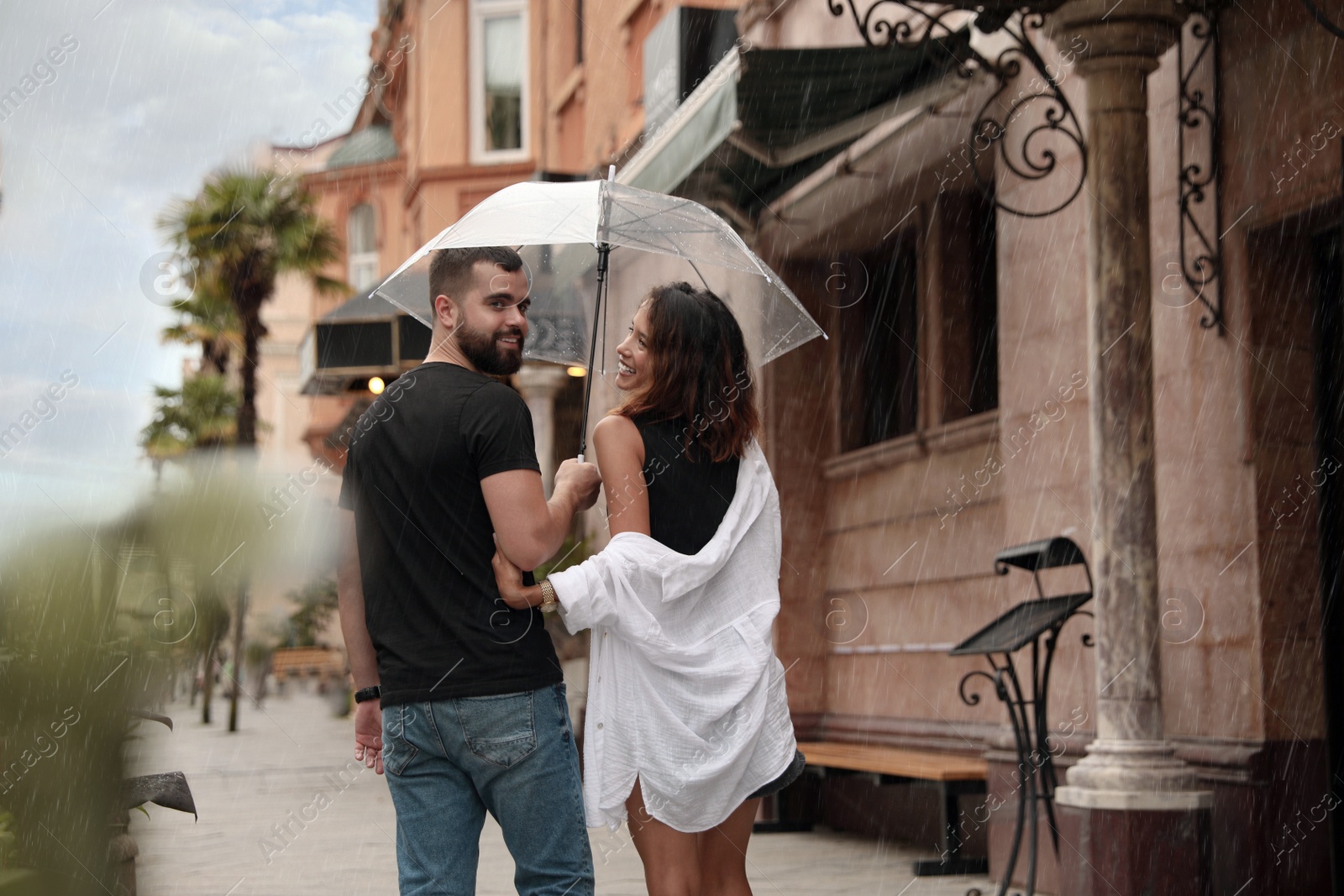 Photo of Young couple with umbrella enjoying time together under rain on city street, space for text