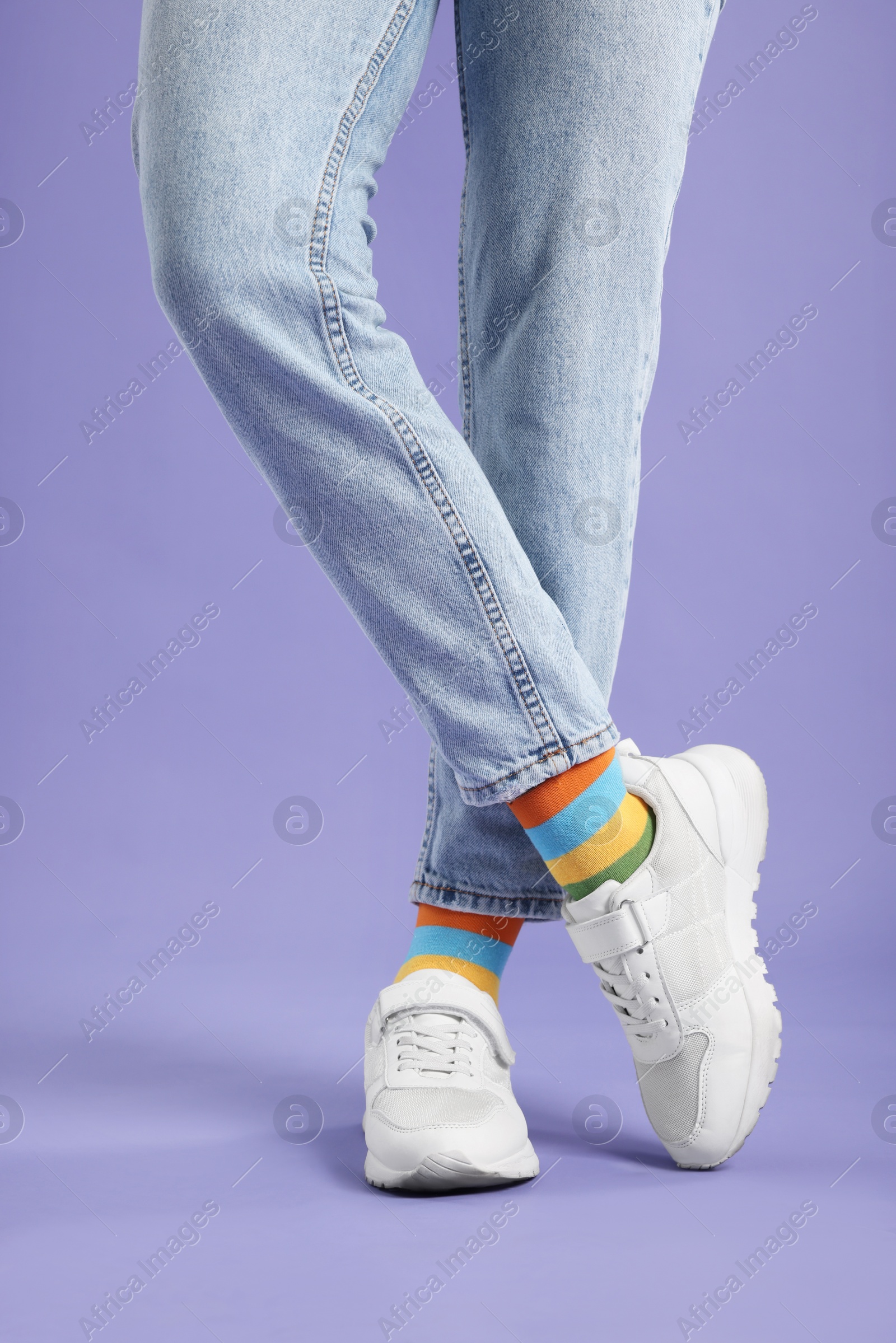 Photo of Woman in stylish colorful socks, sneakers and jeans on violet background, closeup