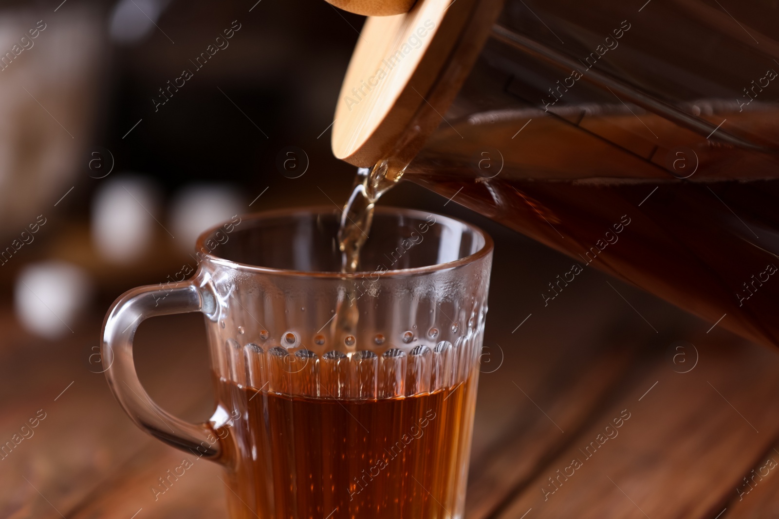 Photo of Pouring delicious tea into glass cup on blurred background, closeup