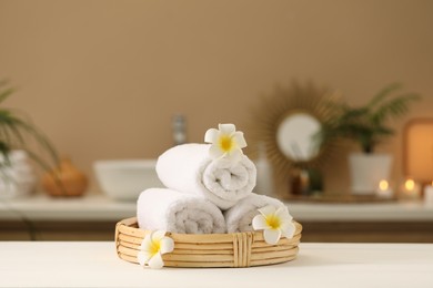 Photo of Spa composition. Rolled towels and plumeria flowers on white table indoors