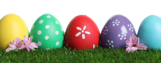 Colorful Easter eggs and flowers on green grass against white background