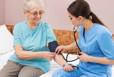 Nurse measuring senior woman's blood pressure in hospital ward. Medical assisting