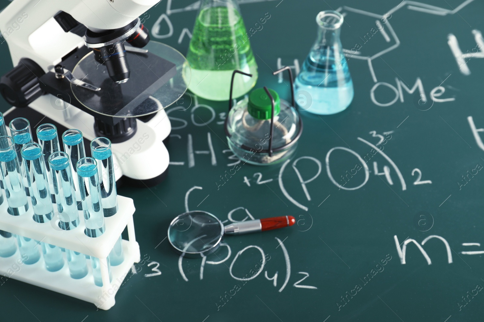 Photo of Laboratory glassware and microscope on blackboard with chemical formulas